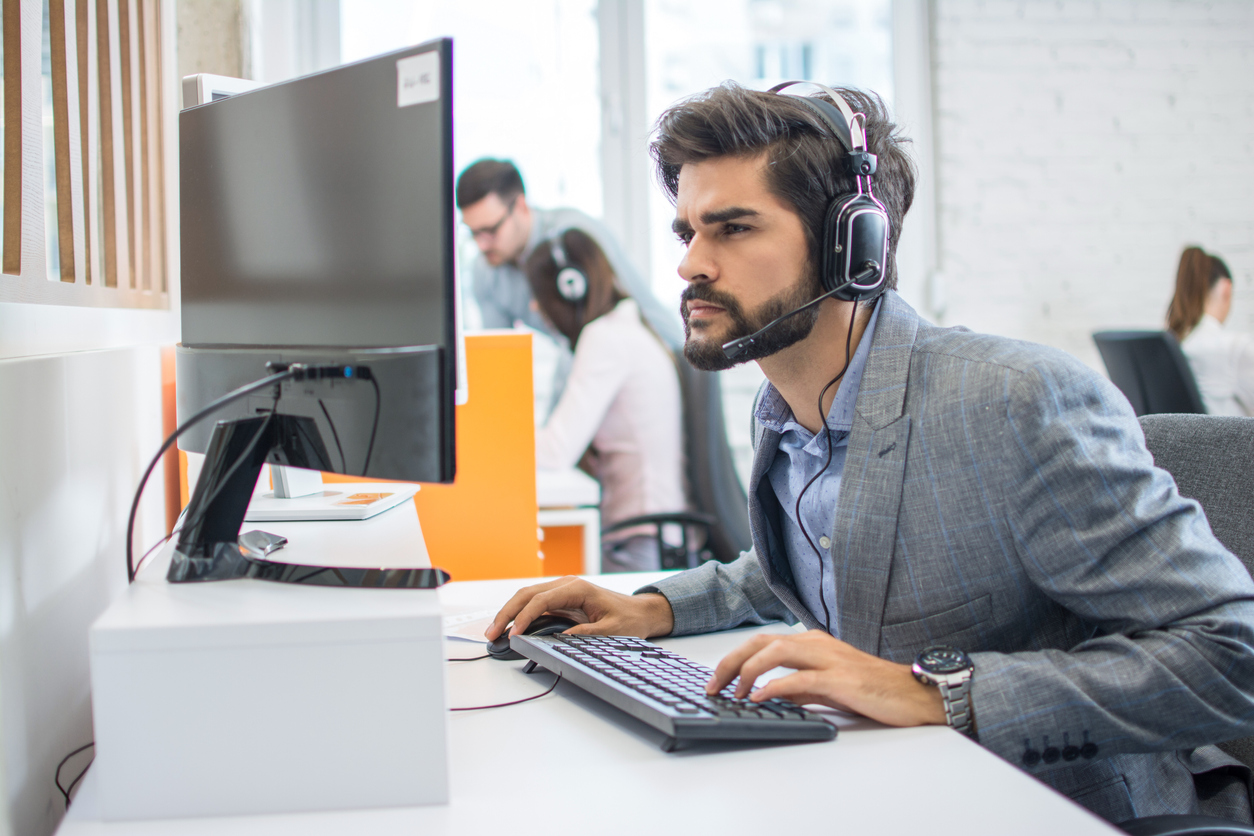 A young male customer service agent peers intently at a computer screen.