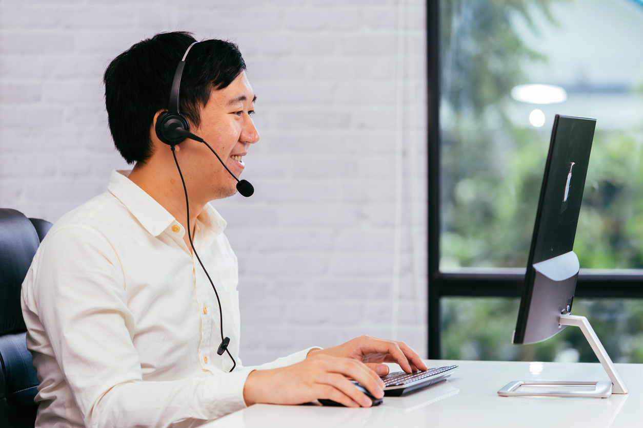 Male contact center agent sitting at a computer and talking on a headset phone