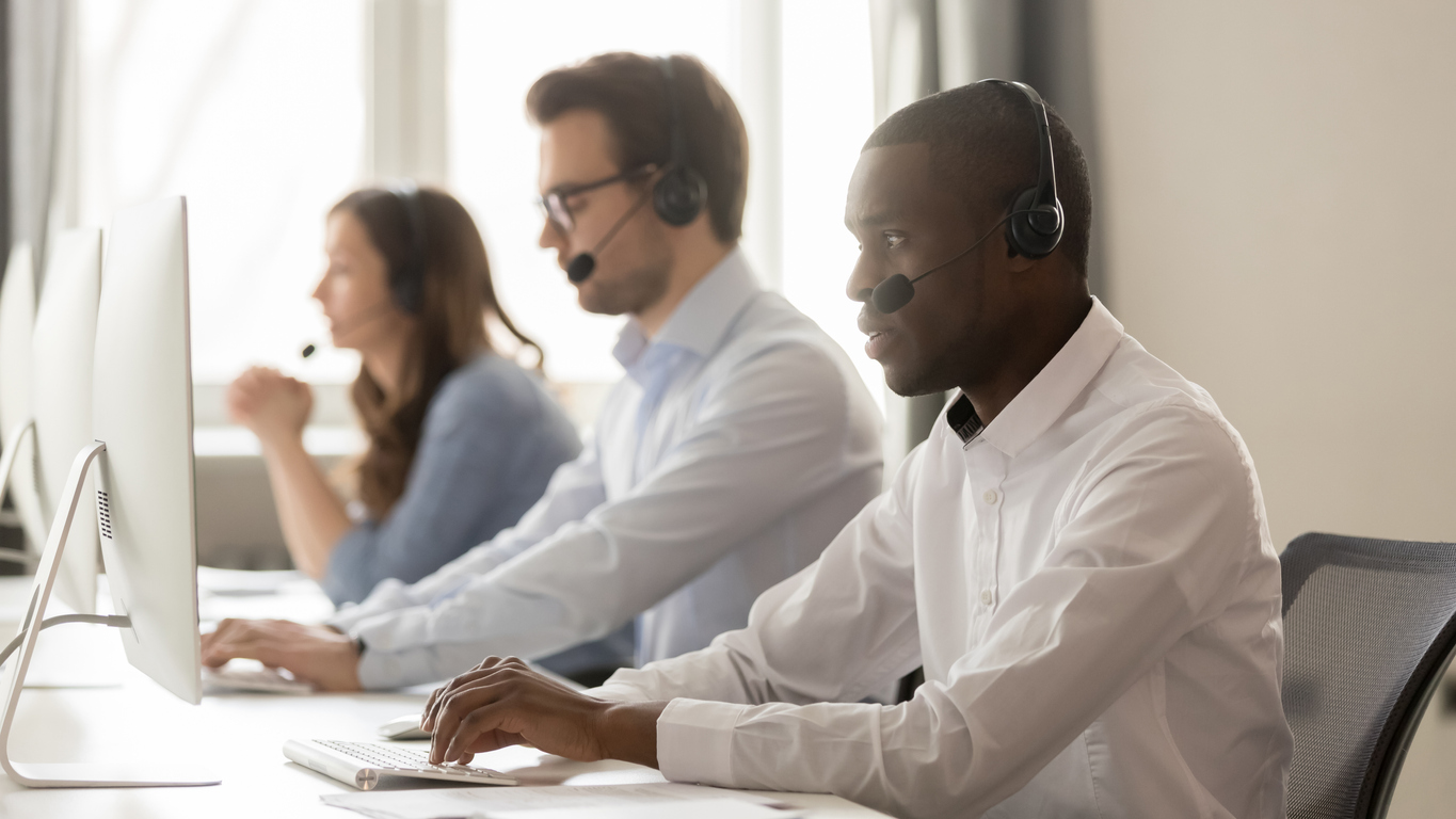 Three contact center agents, with each wearing a wireless headset and working on a computer