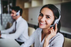 This image shows a smiling female call center worker with another worker in the blurred background. 