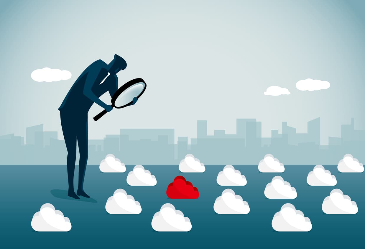 This image is a drawing of a man in a business suit with a large magnifying glass. He’s standing in front of a backdrop of a cityscape, and in front of him are a number of clouds; one of them is red, the others are white. This represents making a choice of cloud service providers.