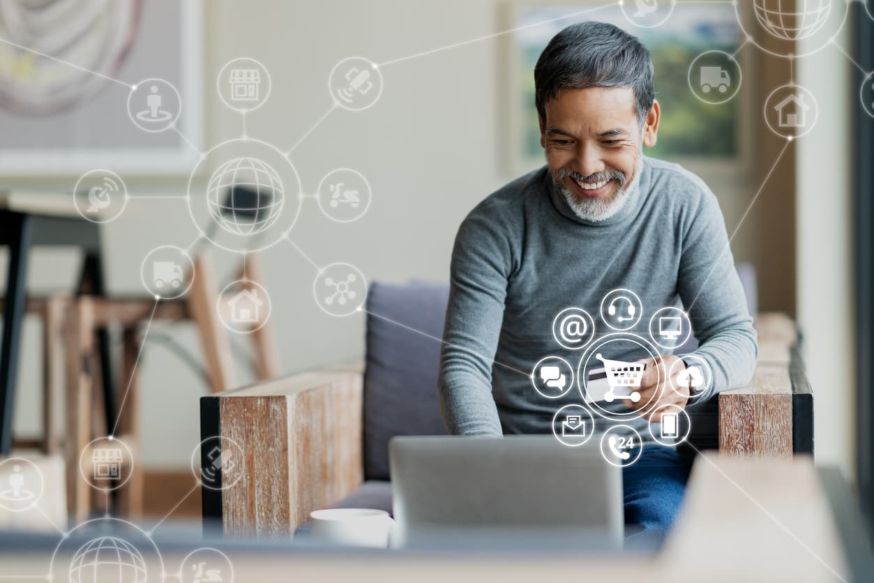 A man sits at his laptop with credit card in hand. He’s smiling, and his other hand is on the keyboard. He’s surrounded by icons for customer service, e-commerce, mobile, chat, phone, and the cloud.