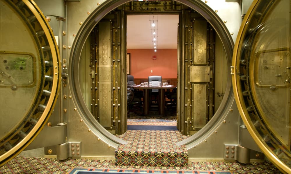 Large gold bank vault open and showing a conference table and work devices inside.