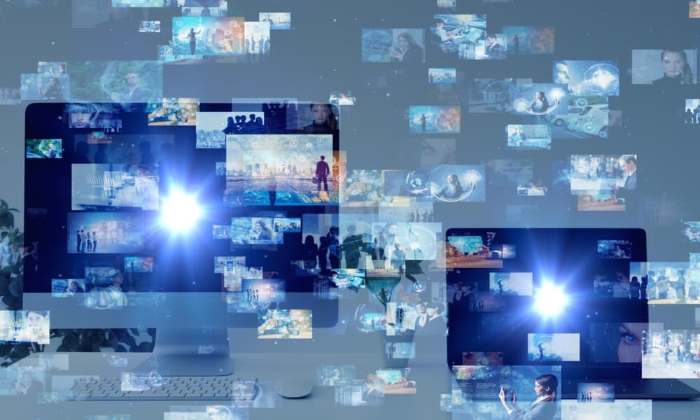 Two computer monitors show a bright white light radiating from the center. Surrounding and superimposed on the monitors are images of people in various situations – in the office, on a beach – using various devices.